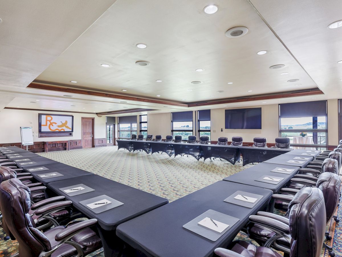 A spacious conference room with U-shaped table setup, leather chairs, projection screen, and bright lighting.