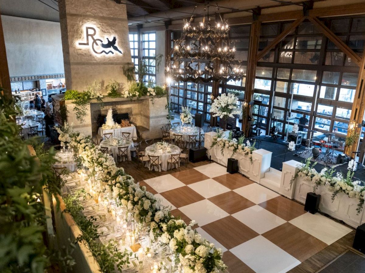 A beautifully decorated event space with elegant floral arrangements, a checkered dance floor, and chandeliers, creating a sophisticated ambiance.