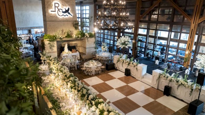 A beautifully decorated event space with elegant floral arrangements, a checkered dance floor, and chandeliers, creating a sophisticated ambiance.