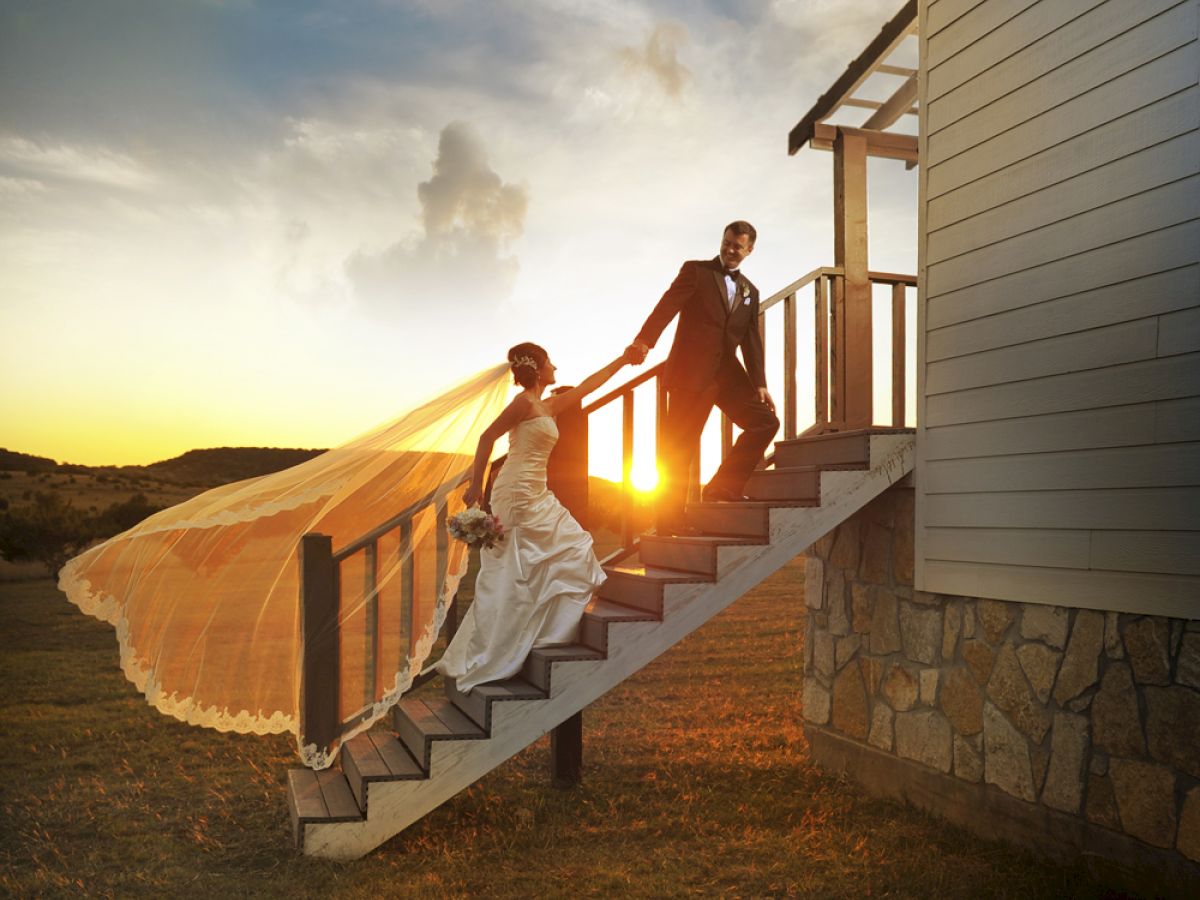 A bride and groom descend outdoor stairs at sunset, with the bride's veil flowing in the wind, capturing a picturesque moment.