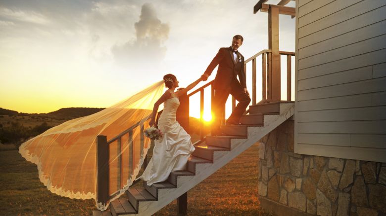 A bride and groom descend outdoor stairs at sunset, with the bride's veil flowing in the wind, capturing a picturesque moment.