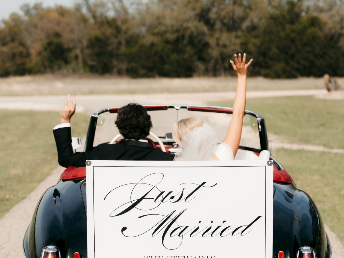 A couple waves from a classic blue convertible wedding car, with a &ldquo;Just Married&rdquo; sign for The Stewarts.
