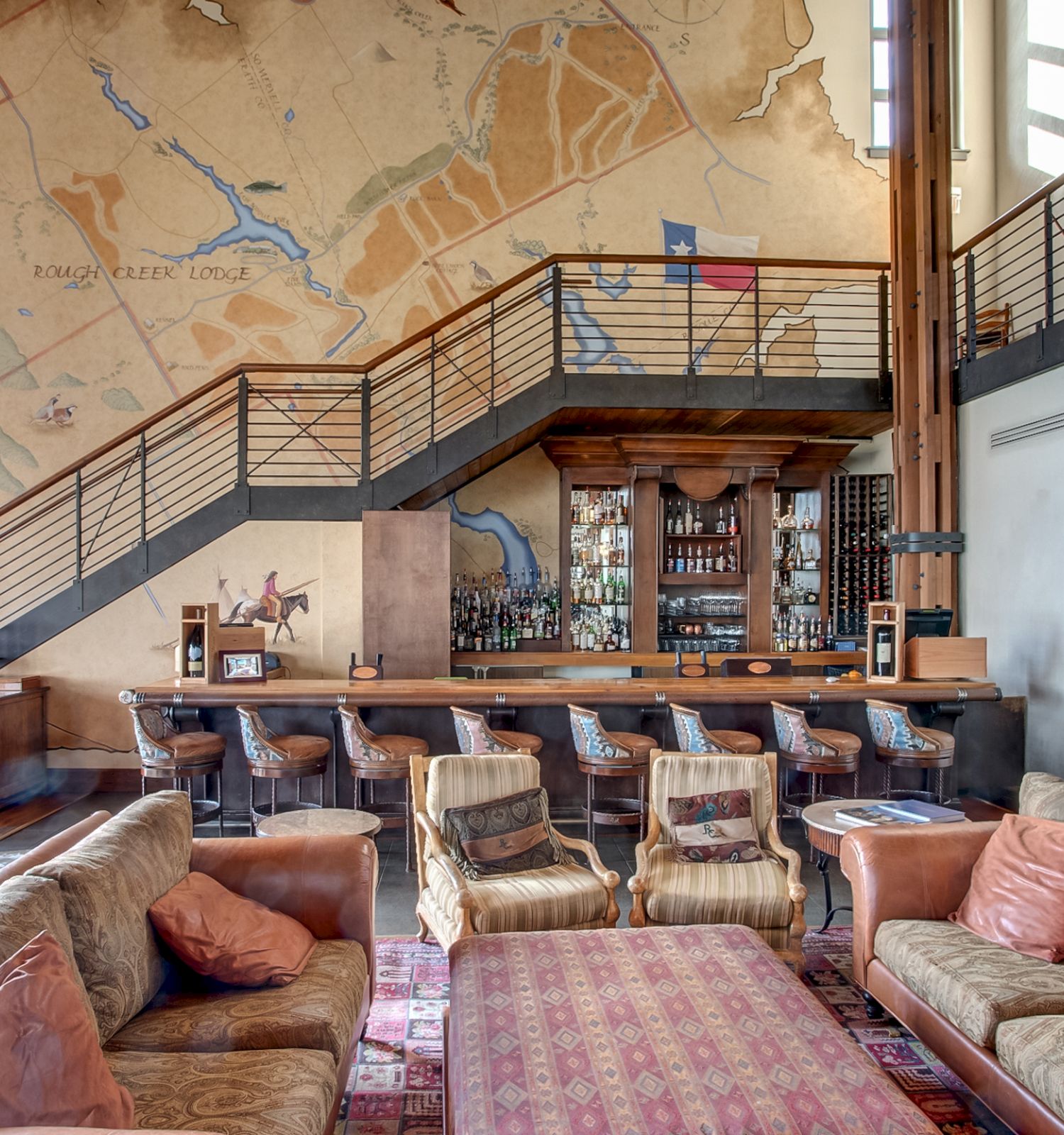 A cozy lounge area with sofas, a bar with high chairs under a staircase, and a large map on the wall.