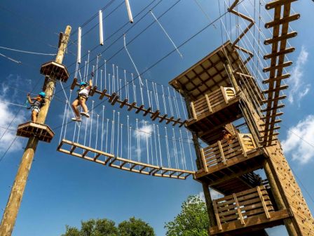 Two people navigating a high ropes course with platforms and ladders under a clear blue sky.