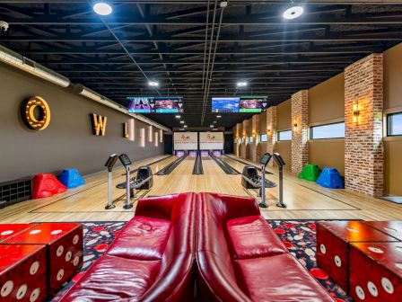 Indoor bowling alley with neon lanes, red leather seating, ball returns, and colorful bumper ramps.