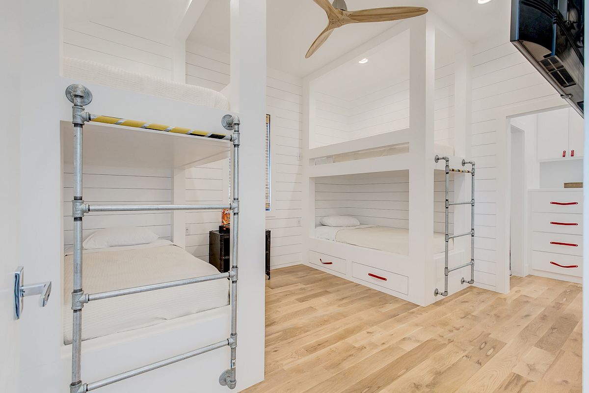 A modern bedroom with built-in bunk beds, wood flooring, and white walls. A ceiling fan is visible, with red accents on drawers.