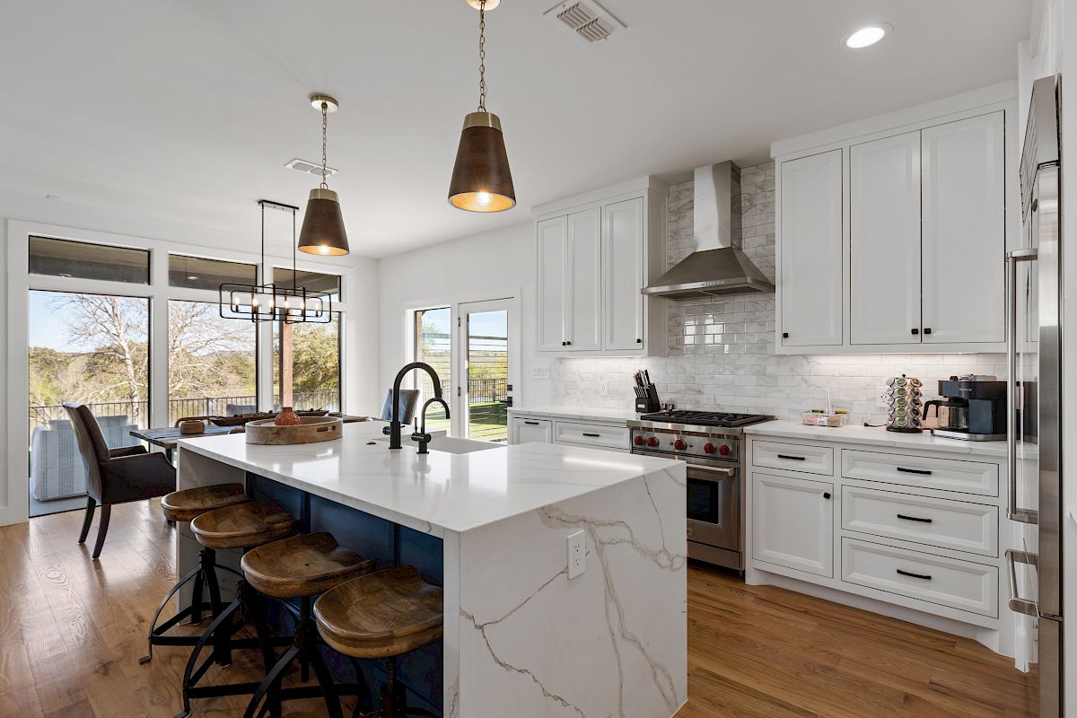 A modern kitchen with white cabinets, an island with barstools, and stainless steel appliances.