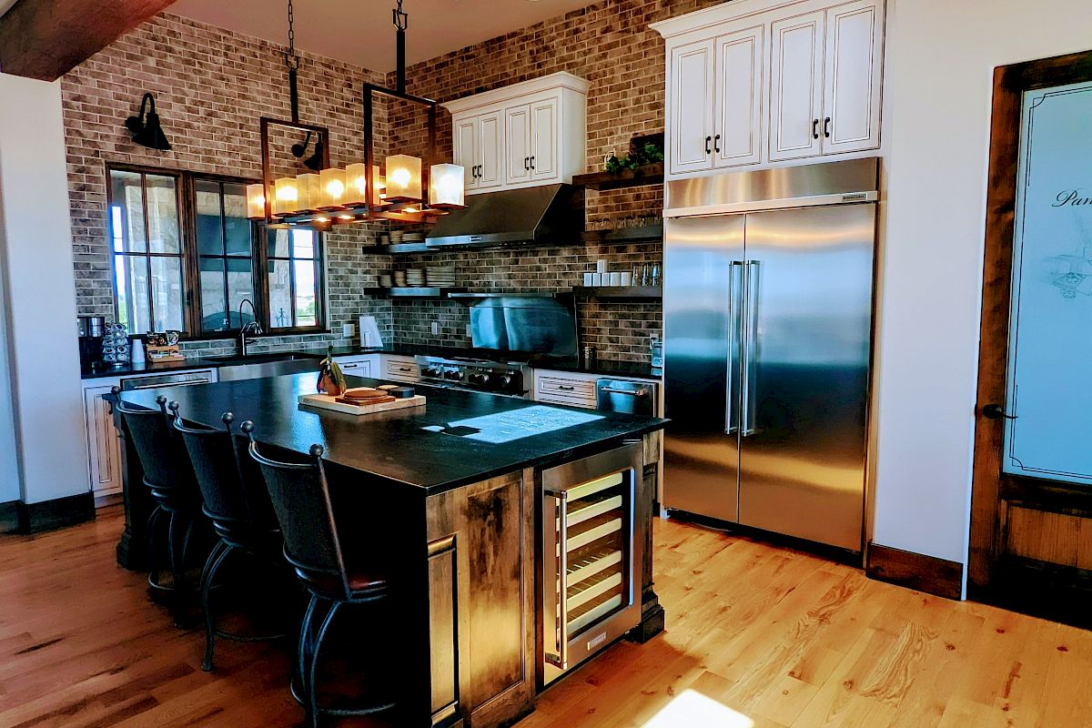A modern kitchen with wooden floors, exposed beams, a skylight, island, and stainless steel appliances under pendant lighting.