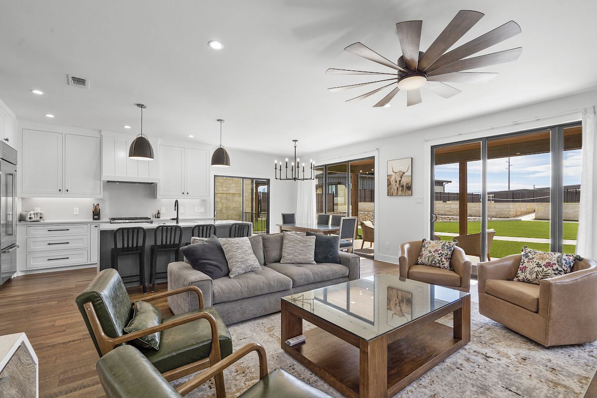 A modern open-plan living room and kitchen with stylish furniture, large windows, and a ceiling fan.