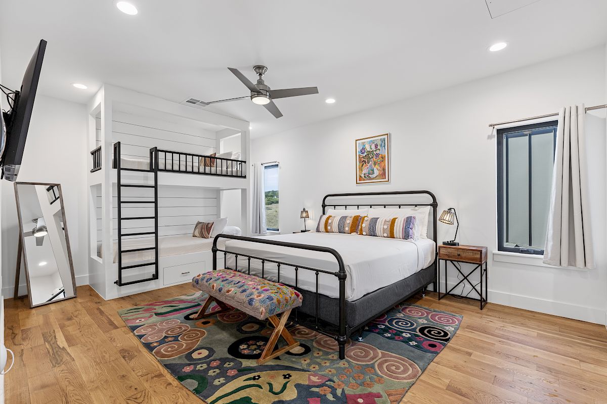 A bedroom with a double bed, bunk beds, and colorful decor, featuring a ceiling fan and wall art in a bright setting.