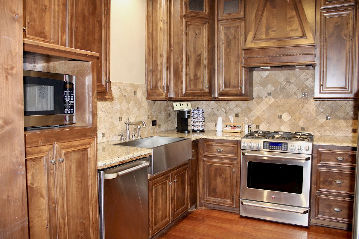 A kitchen with wooden cabinets, a stainless steel oven, microwave, dishwasher, and sink, plus a counter with a coffee machine and cups.