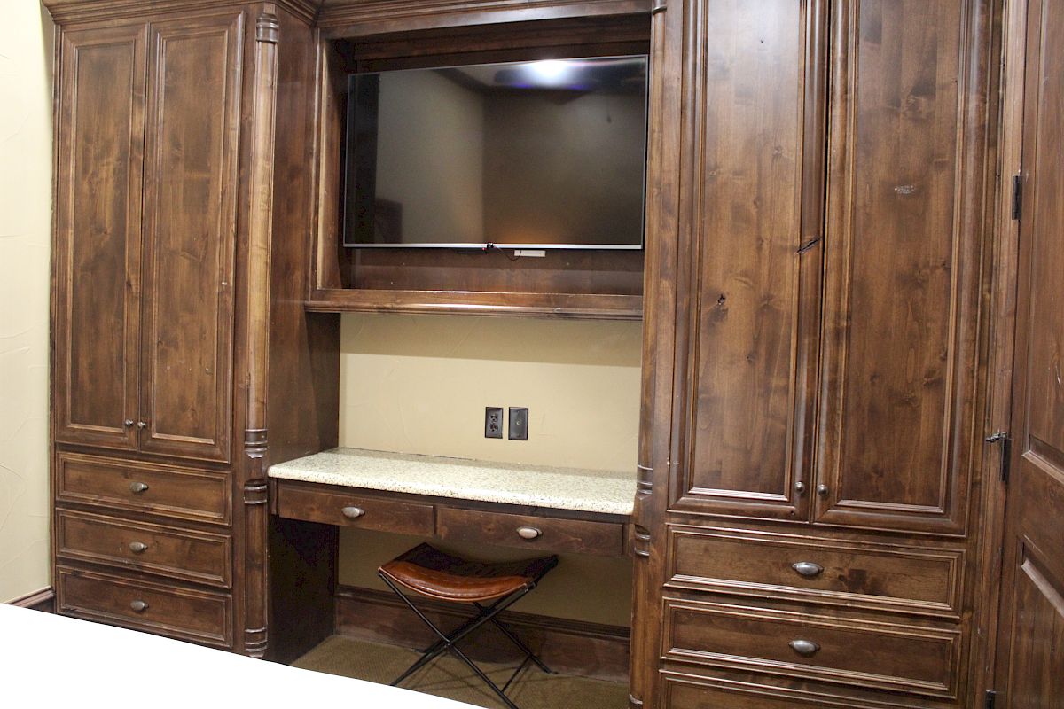 A wooden cabinet with a mounted TV, drawers, and a marble desk with a stool underneath.