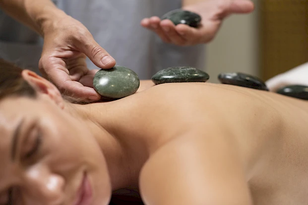 A person receives a hot stone massage with smooth, dark stones placed along their back for relaxation and therapy.