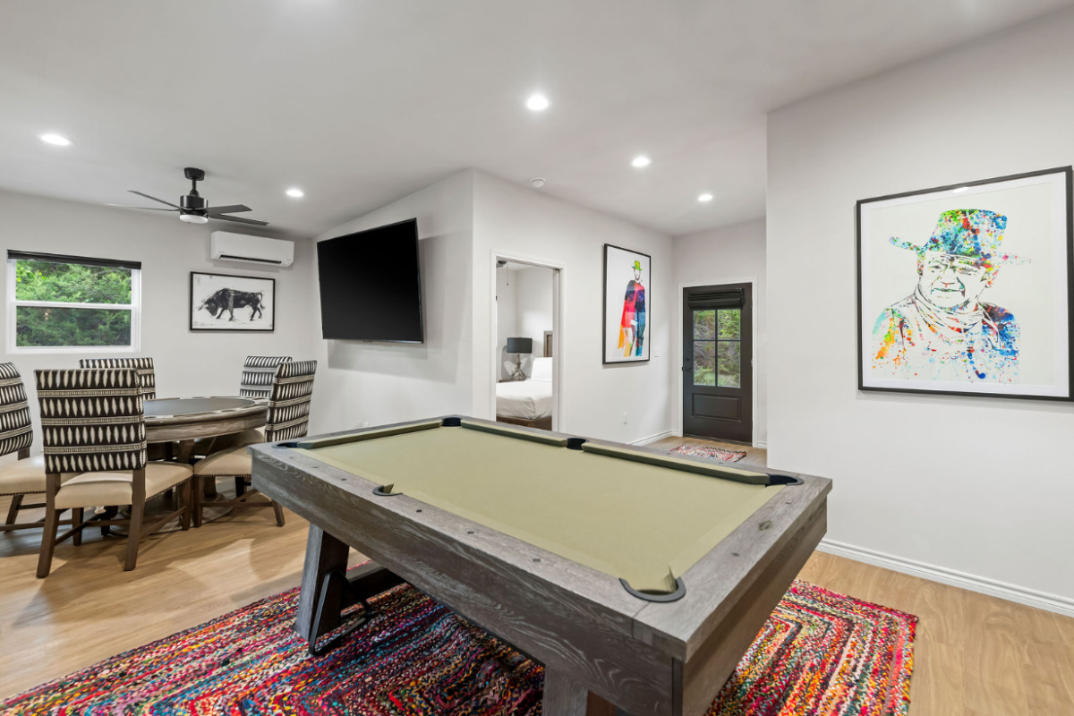A modern game room with a pool/billiards table, TV, colorful rugs, and framed art on white walls.