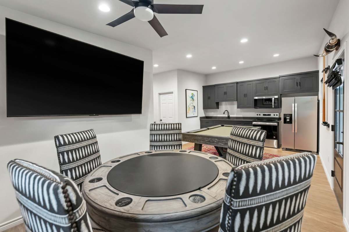 A modern living space with a wall TV, striped chairs, a robot vacuum, and a sleek kitchen with stainless appliances.