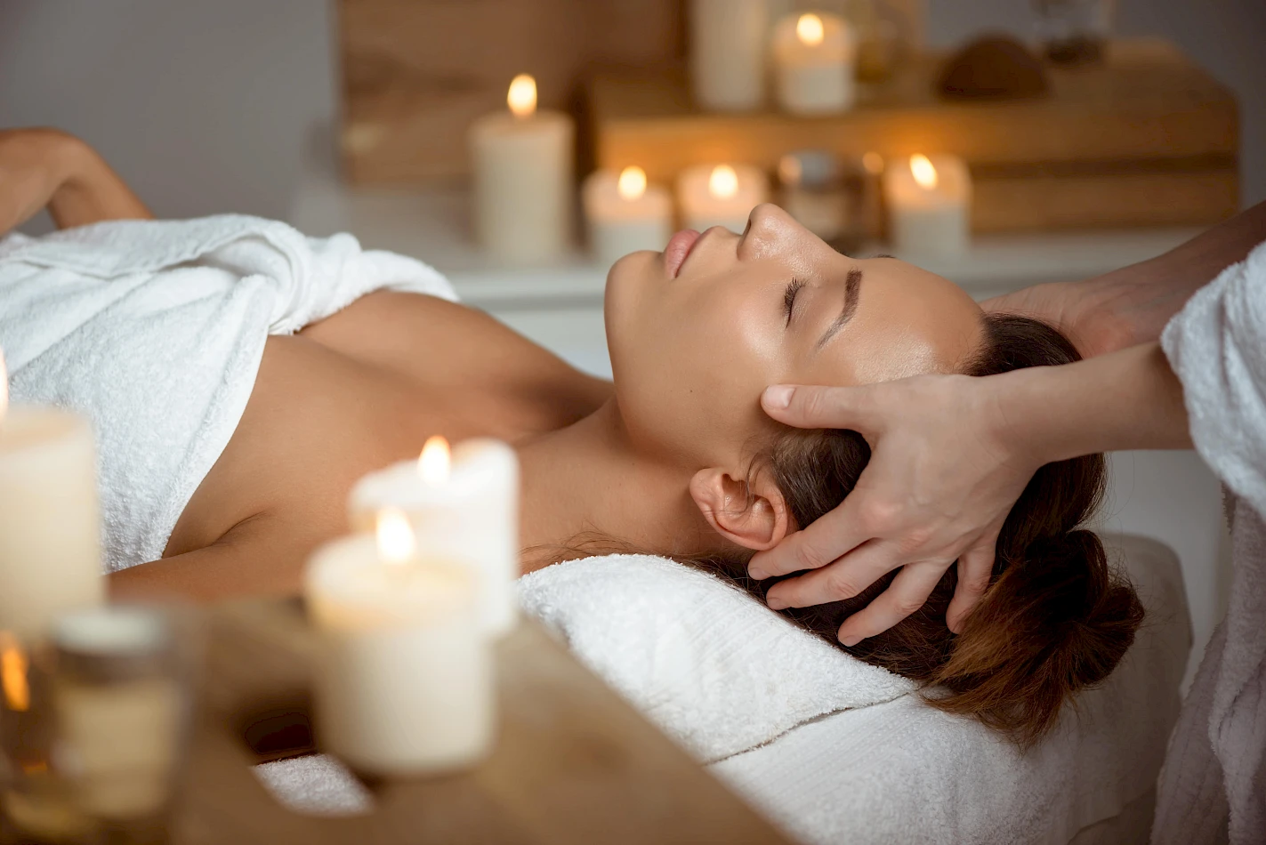 A person is receiving a head massage in a spa setting with lit candles creating a relaxing atmosphere.