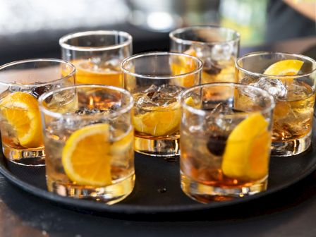 A tray holds seven glasses of cocktails, each garnished with orange slices and ice, creating a refreshing display.