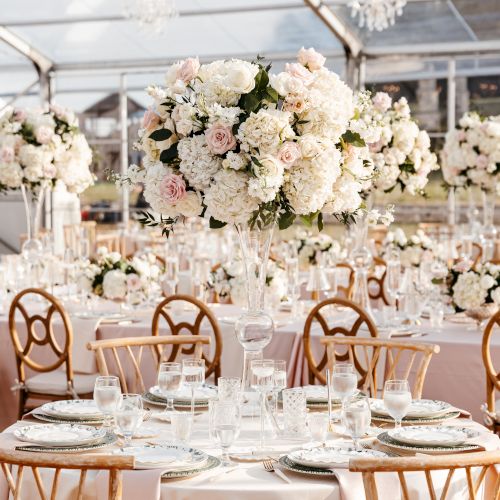 The image shows elegant wedding decor with round tables, floral centerpieces, gold chairs, and a tented venue, creating a romantic atmosphere.