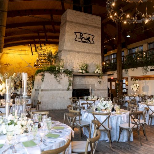 A beautifully decorated indoor venue with elegant dining tables, floral arrangements, a large centerpiece, and a chandelier overhead.