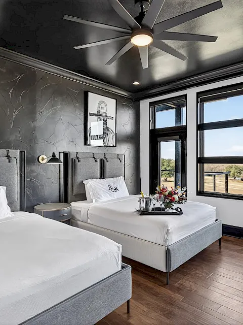 Modern hotel room with two beds, wall art, ceiling fan lights, and big windows showing a river view.