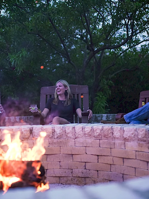 Four people sit around a stone fire pit with a burning fire, relaxing and enjoying each other's company outdoors.