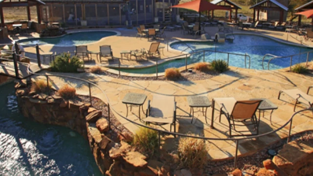 Outdoor leisure area with a pool, chairs, and tables surrounded by a rocky landscape under a clear blue sky.