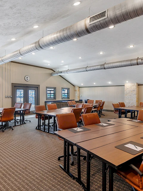 The image shows a modern conference room with tables, chairs, and overhead lighting, creating a professional meeting space.