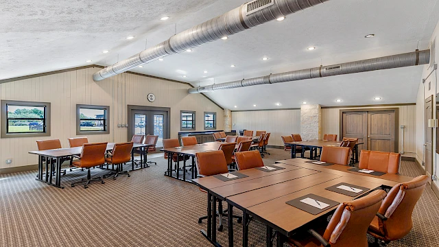 The image shows a modern conference room with tables, chairs, and overhead lighting, creating a professional meeting space.