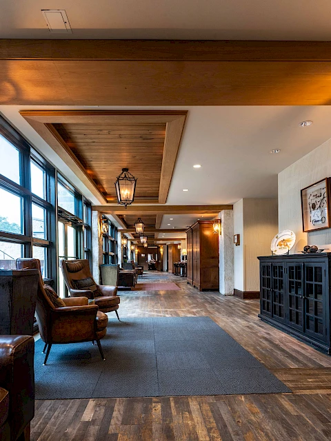 A cozy hallway with wooden floors, armchairs, warm lighting, and large windows, creating an inviting and stylish atmosphere.