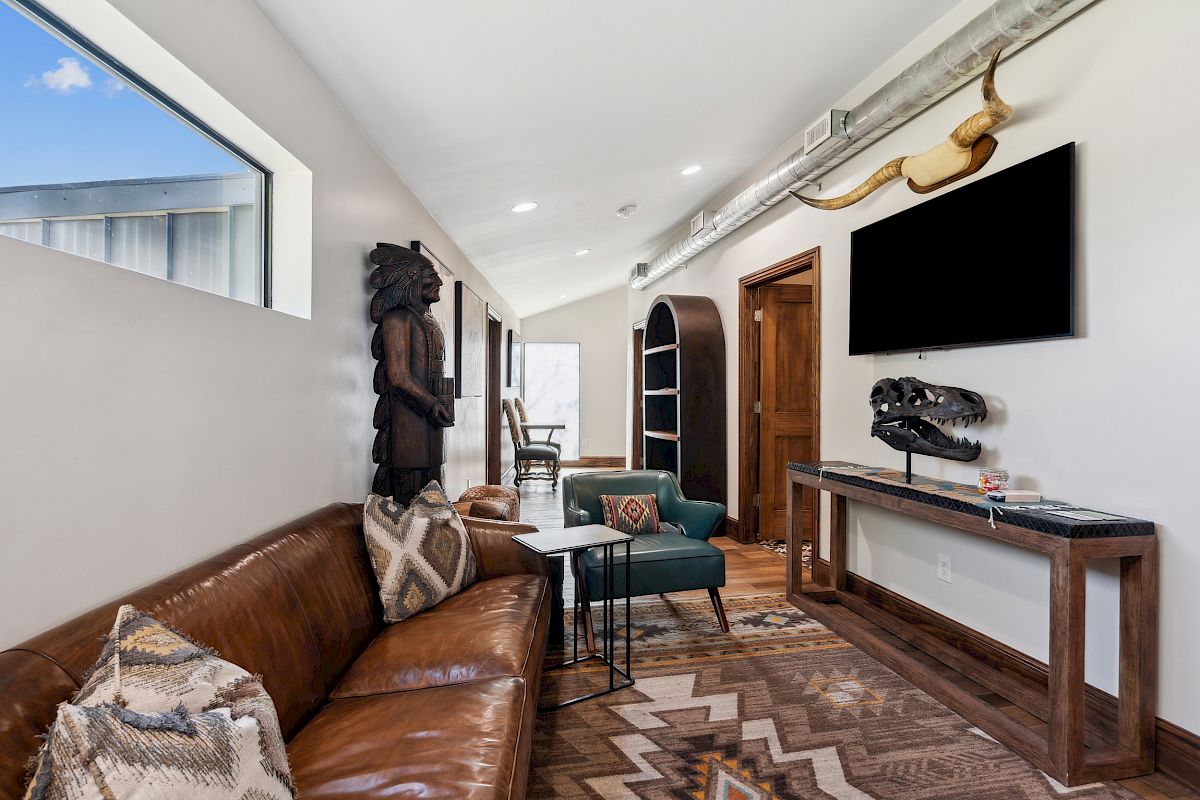 A stylish living room with a brown leather sofa, geometric rug, wall-mounted TV, rustic decor, and a long console table along the wall.