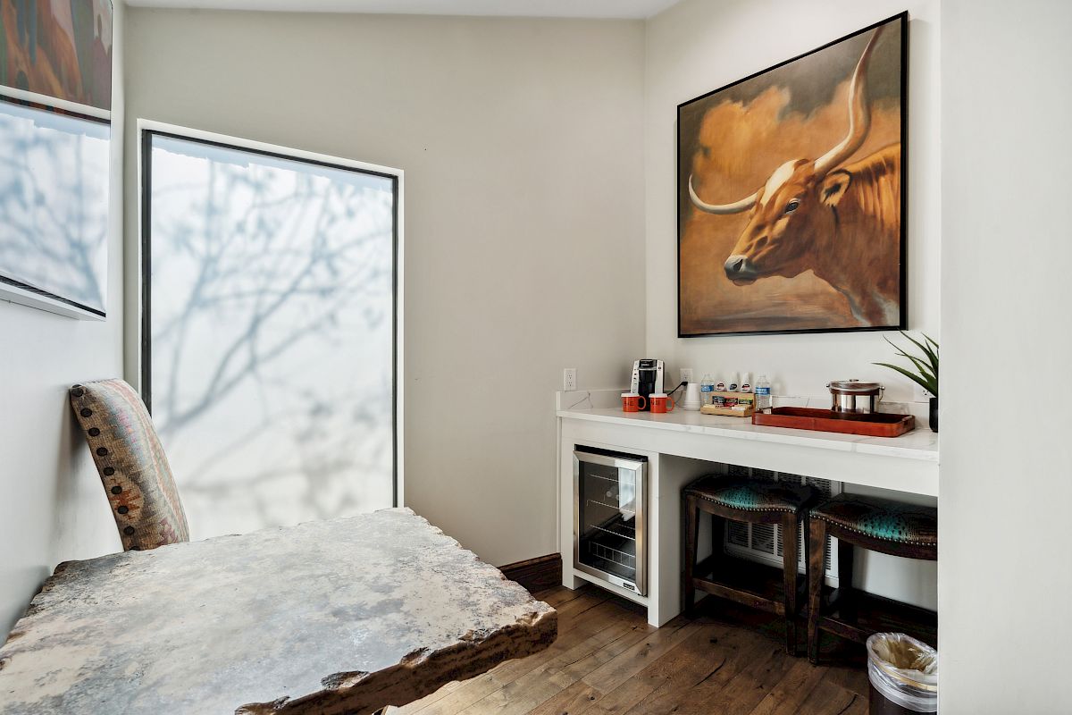 A cozy office or study room with a rustic wooden desk, a large herbivorous animal painting (bull/longhorn) on the wall, and a glass door letting in natural light.