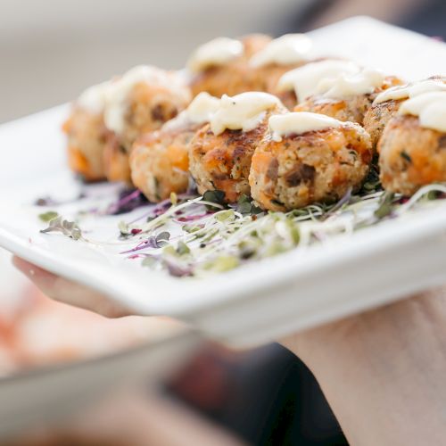 A plate of fried sushi rolls drizzled with sauce, garnished with sesame seeds and greens, ready to be shared.