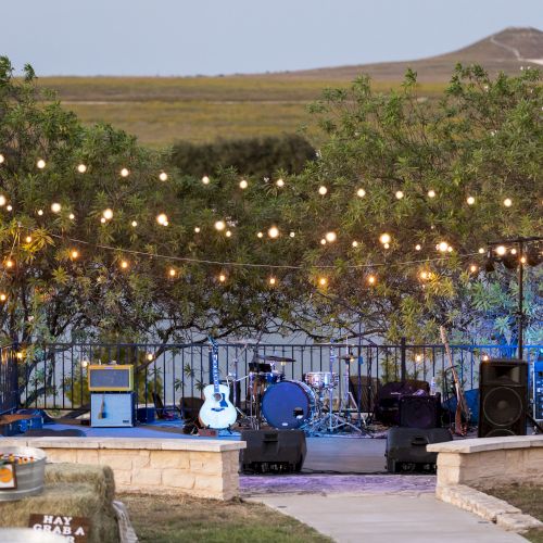 A large outdoor concert or ceremony on a hillside with a stage, colorful lights, and a crowd seated on steps under a clear sky. Top it at 140 characters, always ending the sentence.