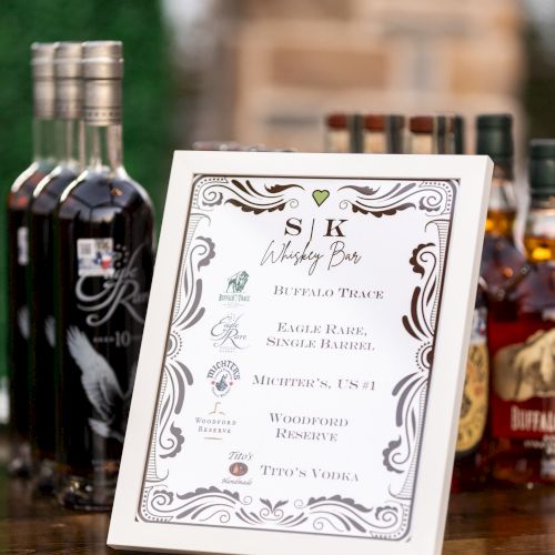 A framed menu or drink list on a bar counter, with bottles (whiskey and soda) in the background.
