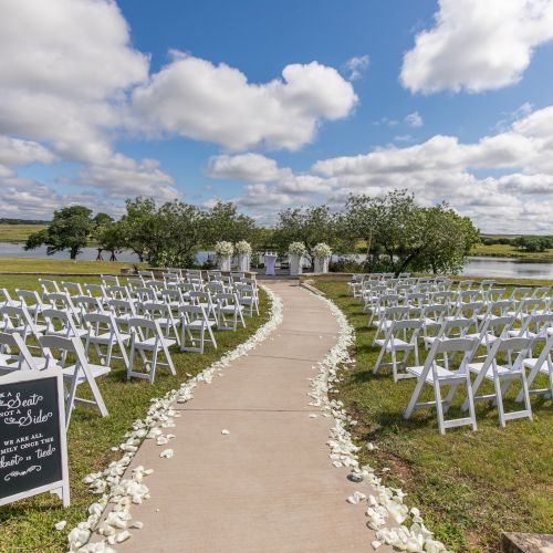 A wooden boardwalk winds through a grassy coastal landscape toward the horizon, with blue skies and distant clouds, ending at a sunny shoreline.