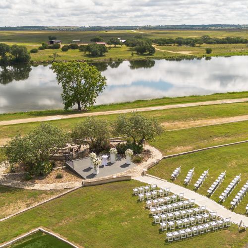 A grassy field with a wooden fence, a small rock area, a few trees in the distance, and a cloudy sky, bordered by a road and open space.