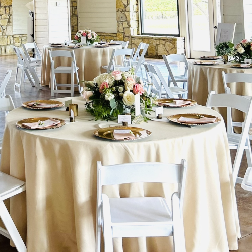 Elegant dining setup with a round table, cream linens, flowers centerpiece, and soft natural light. (Your request ended with a period.)