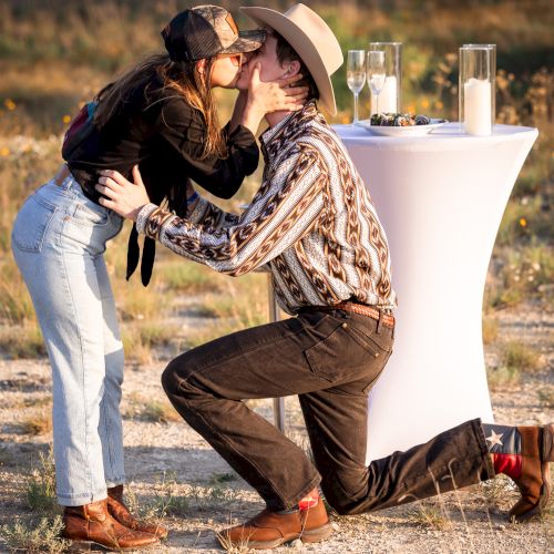 A man and a child share a hug outdoors, with a large white object behind them, on autumn ground.