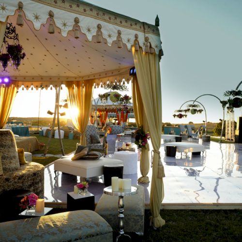 A bright outdoor market or street fair with stalls, people walking, a white tent, colorful shops, and a clear blue sky.