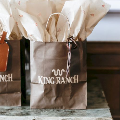 Two white fabric bags labeled &ldquo;SOURCING BRANCH&rdquo; sit on a wooden stool, with soft, blurred background.