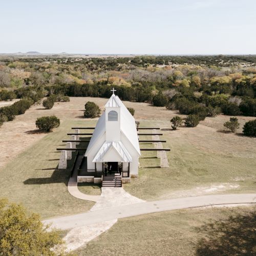 Aerial view of a desert-like park with a white sculpture or structure at the center, surrounded by sparse trees and paths, under a clear sky.