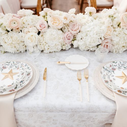 A table with a row of small, ornate pastries or cookies arranged on plates, plus a white fondant cake with decorative icing.