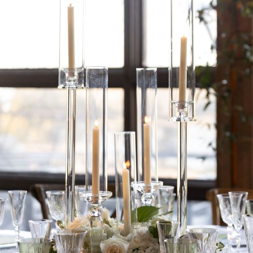 A table set for a formal meal by a window, with candles, glassware, and floral centerpieces, creating an elegant dining scene.