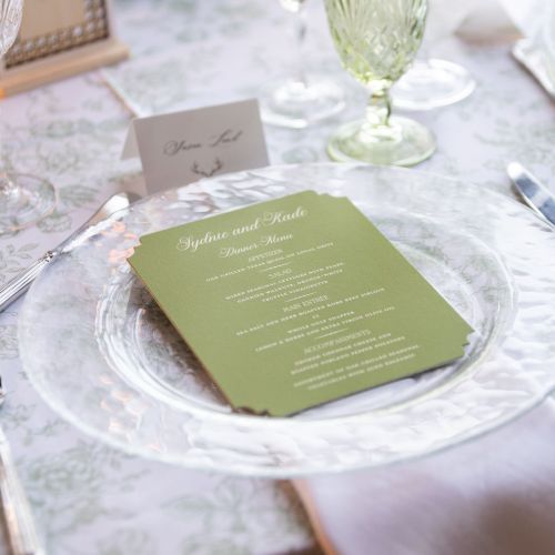 A close-up of a glass and a green slate or coaster on a marble table, with a blurred glass and tableware in the background, indoors.
