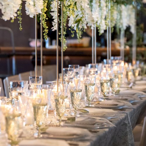 A dinner setting with long table, white napkins, candles, and hanging greenery creating an elegant outdoor banquet ambiance.