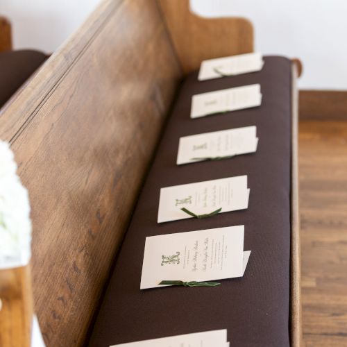 A wooden church pew with small white folded notes or cards placed on the dark padded seat, arranged in a line along the bench.
