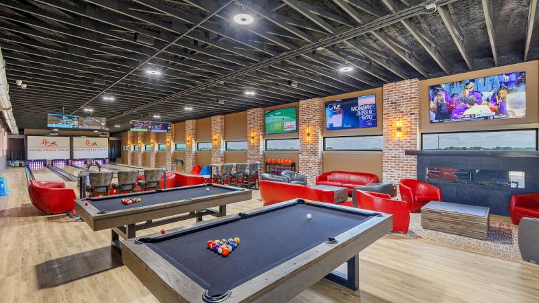 A modern game lounge with two pool tables, red chairs, multiple TVs, and a brick accent wall; a bright, inviting entertainment space ends with clean lines.