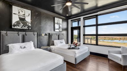 A modern hotel room with two queens, gray upholstered headboards, black-and-white artwork, a large window view, wooden floors, and a seating area.