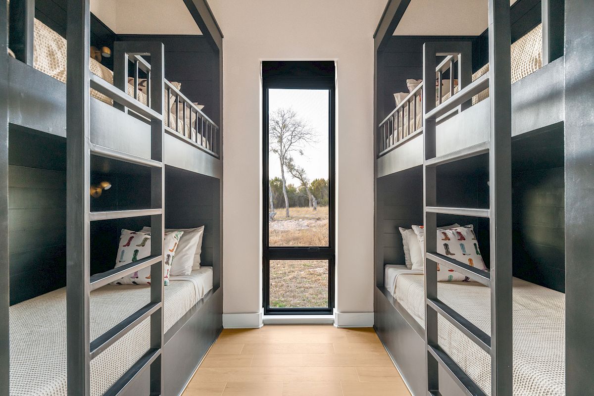 Six bunk beds line both walls of a narrow dorm-style room with a window at the far end, creating a symmetrical, compact sleeping space.