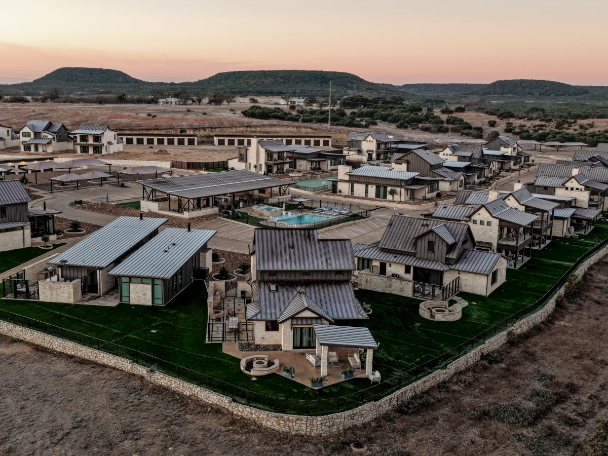 Aerial view of a suburban housing development with many small two-story houses, paved streets, and a central pool, set against a desert-like landscape.